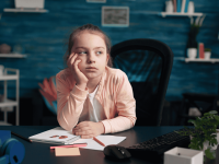 Kind sitzt mit frustriertem Gesichtsausdruck am Schreibtisch