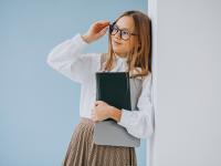Ein schlaues Mädchen lehnt an der Wand mit einem Buch und ihrem Laptop unter dem Arm
