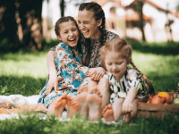 Eine Mutter sitzt lachend mit ihren Kindern auf einer Picknickdecke im Park