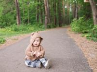 Kleinkind im Bärenkostüm sitzt auf einem Waldweg