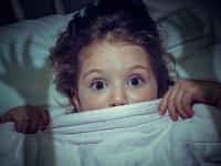 Kind fürchtet sich unter der Bettdecke vor Monstern