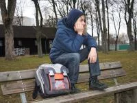 Jugendliche Person sitzt mit Schulranzen auf der Rücklehne einer Bank