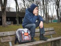 Jugendliche Person sitzt mit Schulranzen auf der Rücklehne einer Bank