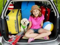 Mädchen mit Hund und Urlaubsgepäck im Kofferraum