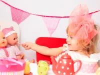 Mädchen füttert eine Puppe umgeben von pinken Accessoires