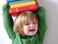 Kind balanciert einen Bücherstapel auf seinem Kopf