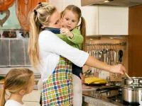 Mutter beim "Multitasken" mit Kindern und Telefon am Herd