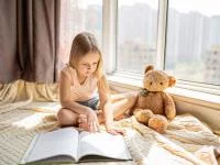 Foto eines Mädchens mit Teddy beim Lesen