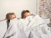Kinder liegen verschreckt unter der Bettdecke