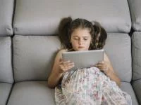 Mädchen lümmelt mit Tablet auf dem Sofa